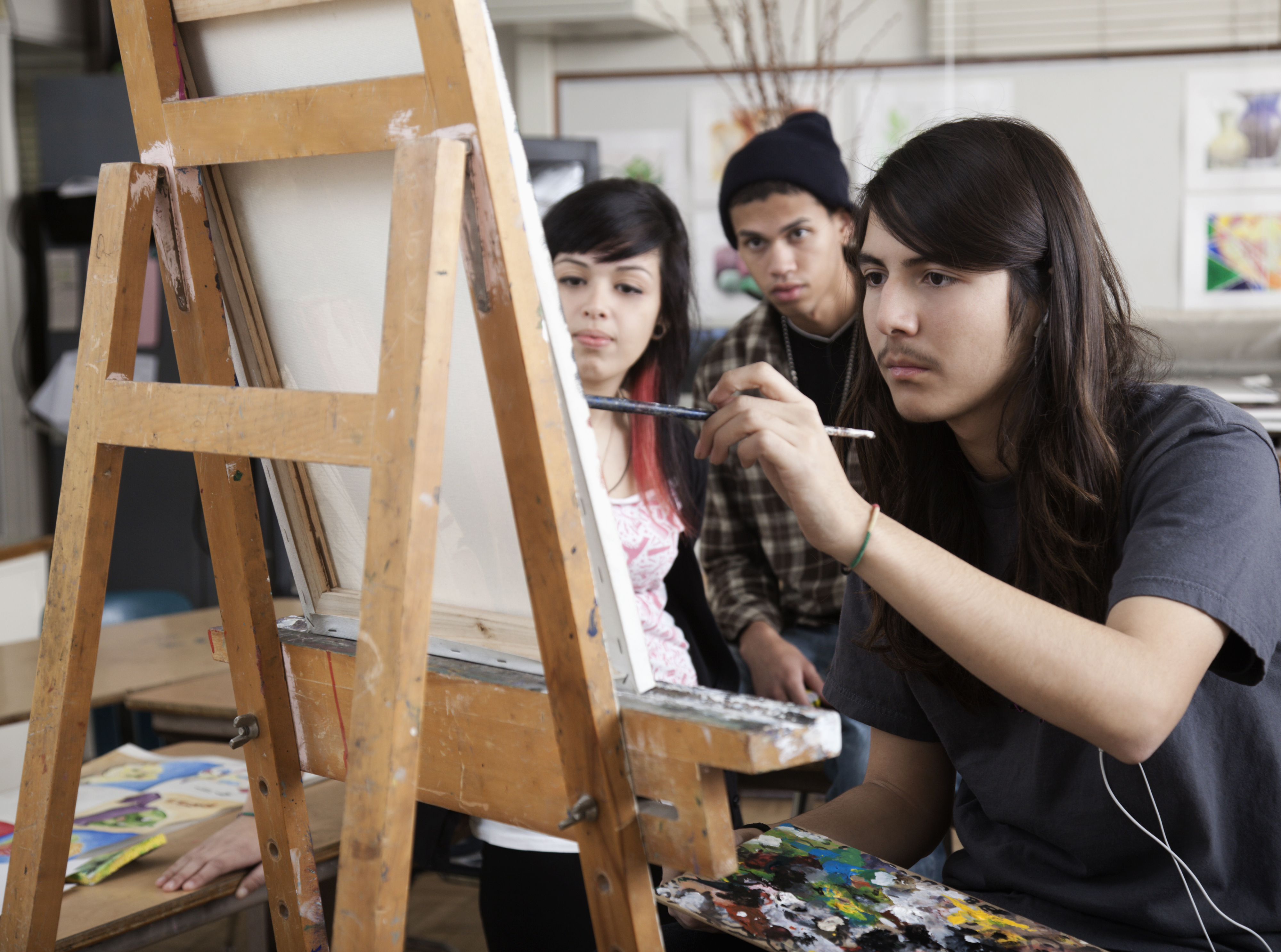 Three artists focus intently on painting at easels in an art studio