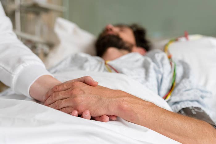 Person holding the hand of a patient resting in a hospital bed