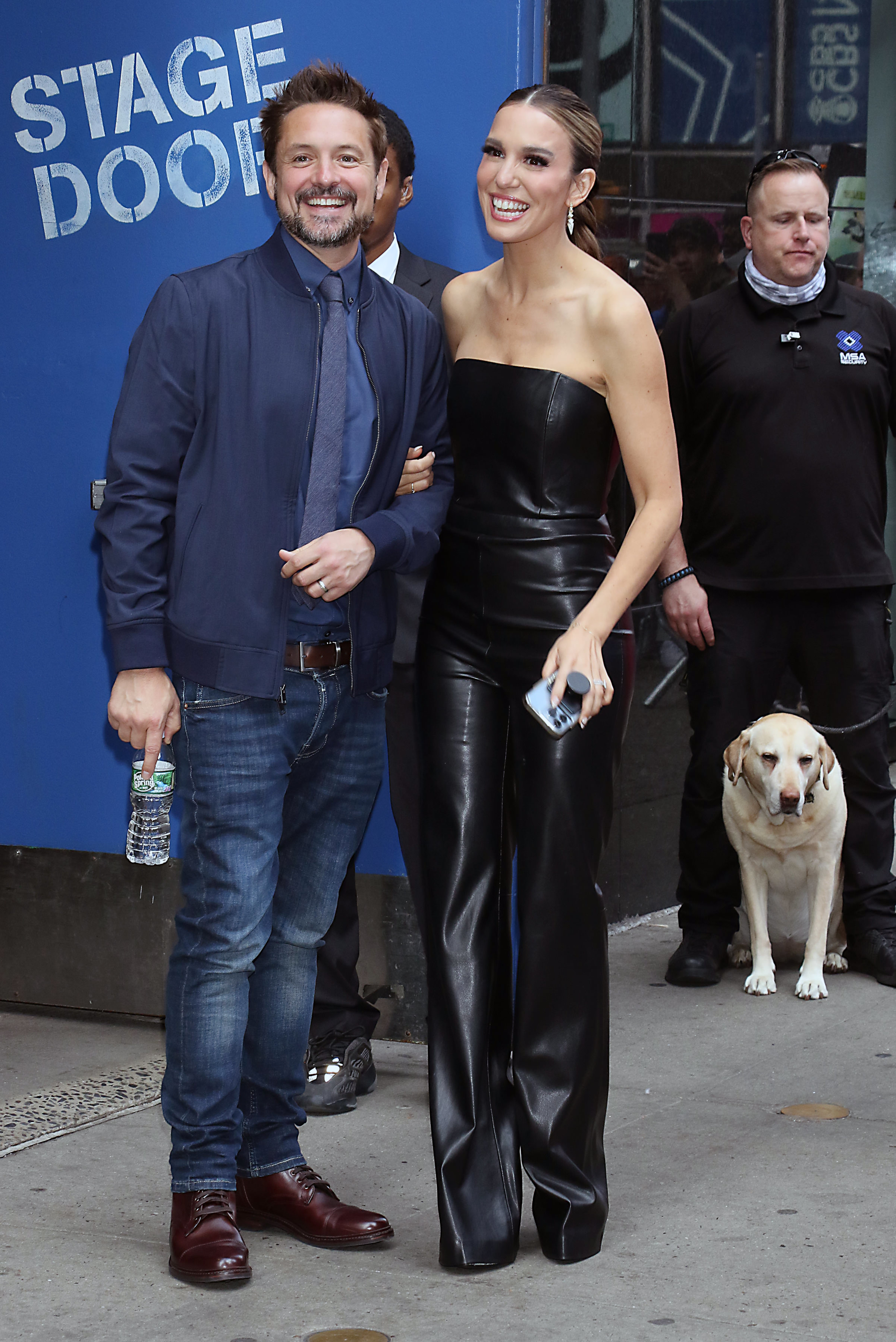 Will Friedle and Christy Carlson Romano stand together outside with their arms linked. Johansson is wearing a strapless leather jumpsuit, with a dog beside them