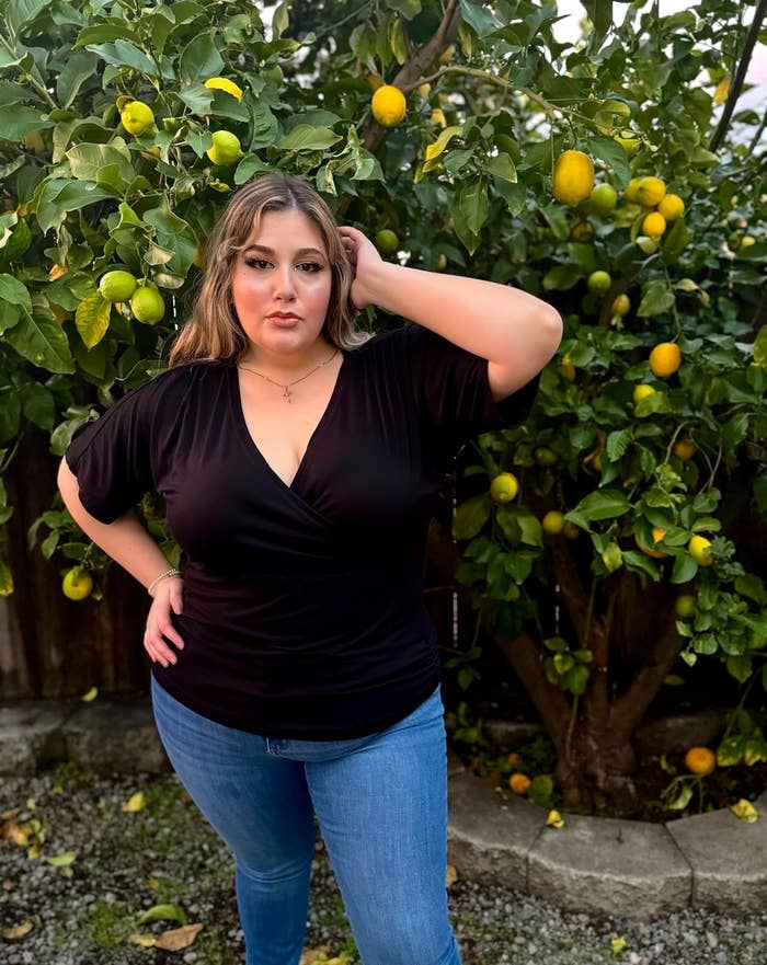 Reviewer posing in a tunic v-neck top and jeans in front of a lemon tree