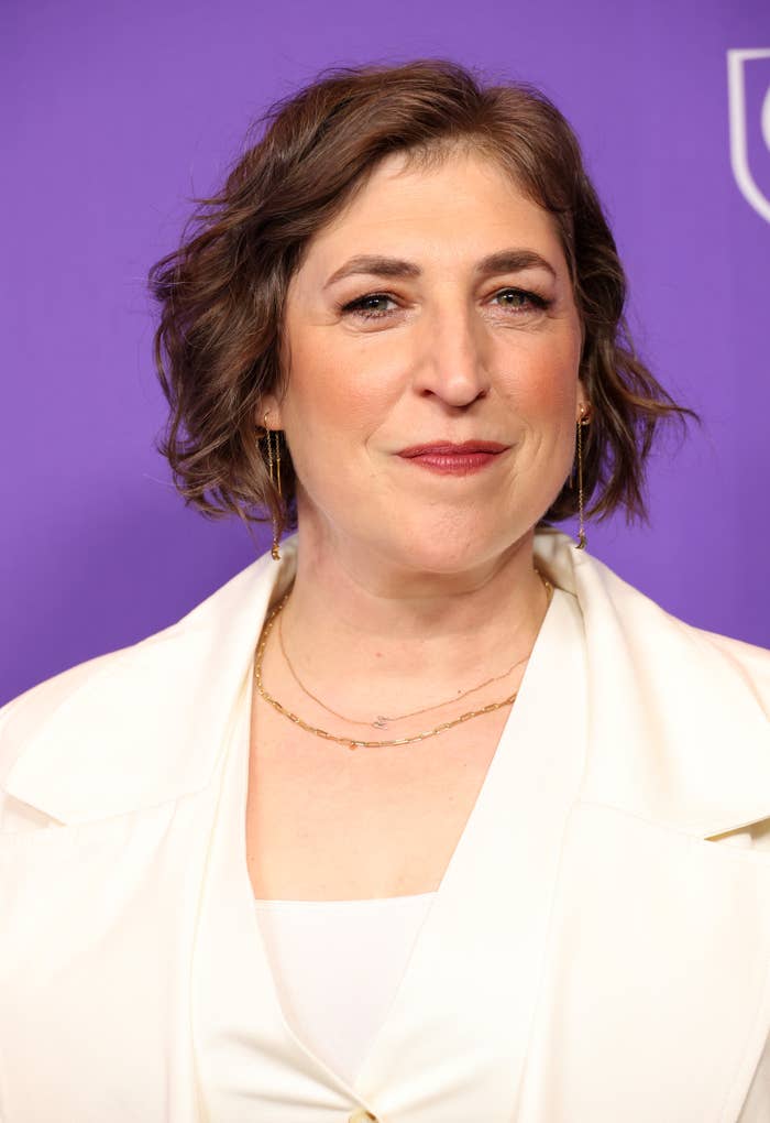Mayim Bialik wearing a stylish outfit featuring a jacket and a thin necklace at an event