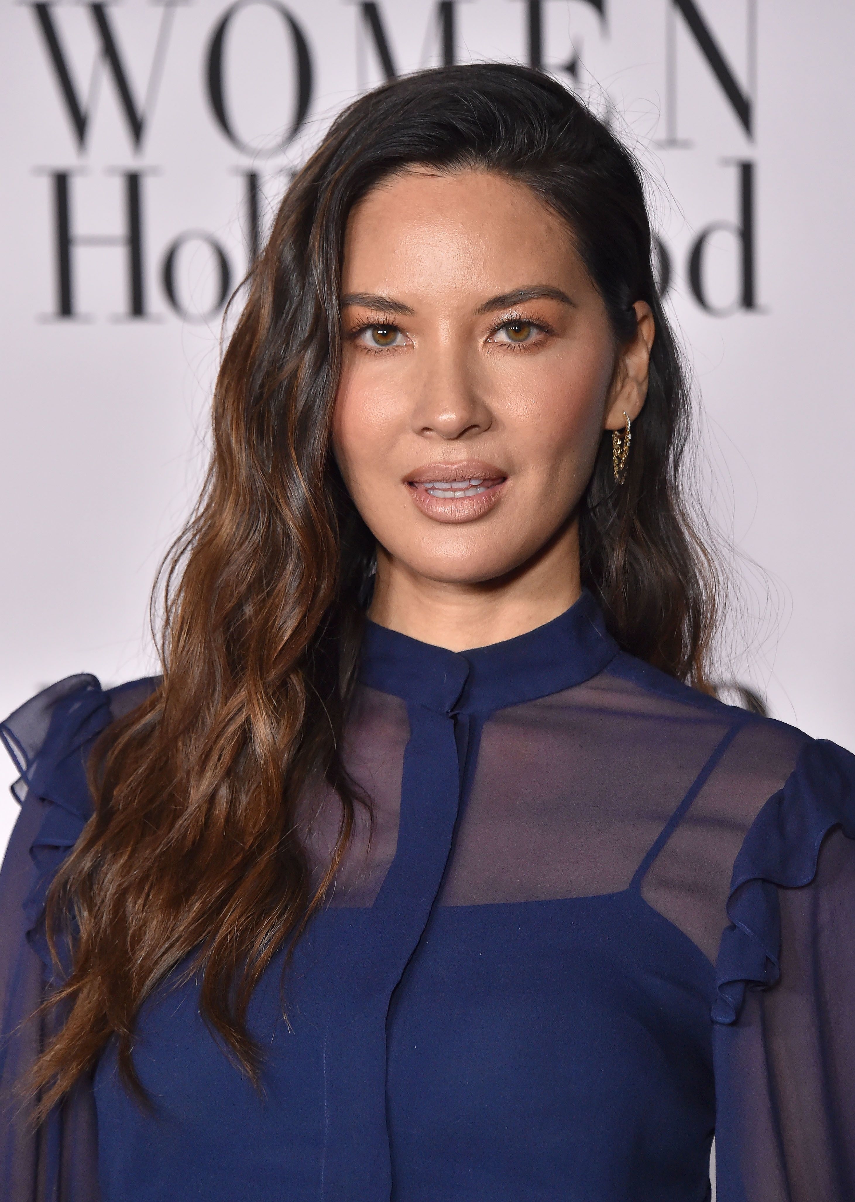 Olivia Munn in a sheer-sleeved blouse posing for a photo