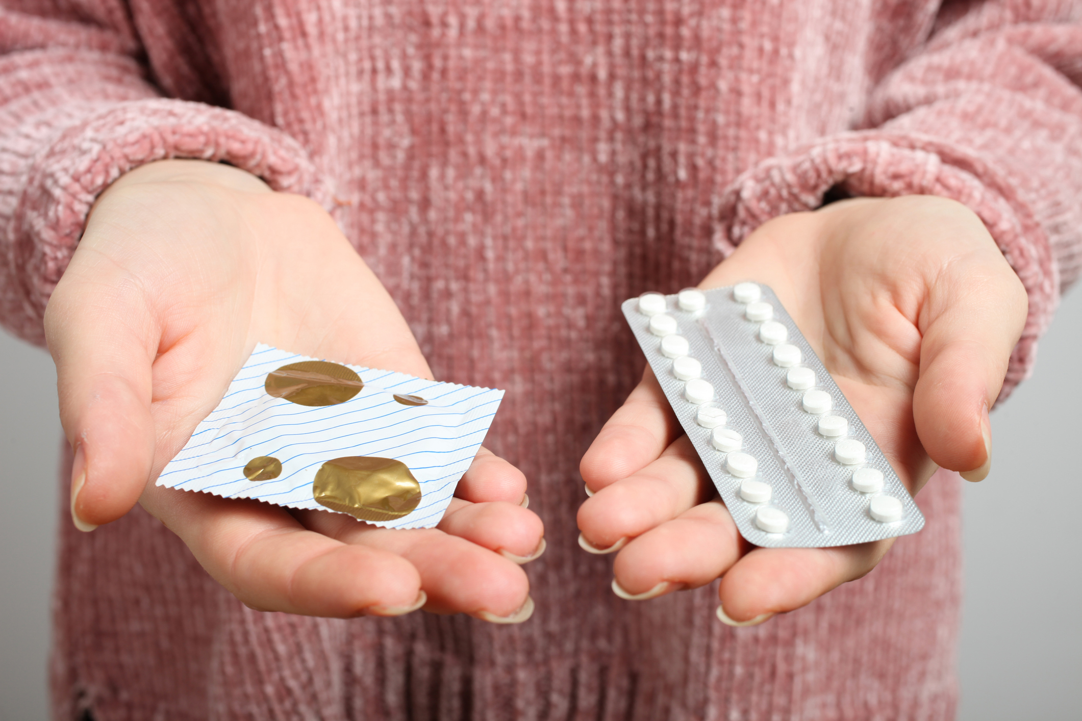 Person holding a blister pack of pills and a condom package