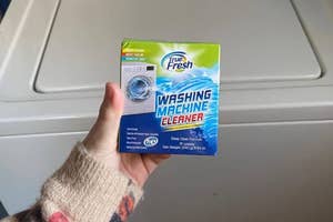 Person's hand holding a box of True Fresh Washing Machine Cleaner by a washing machine