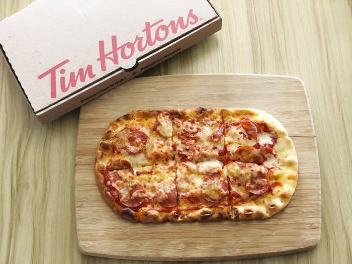 Pepperoni pizza on a wooden board next to a Tim Hortons box