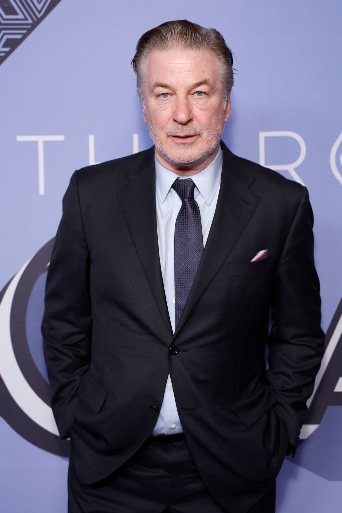 Alec Baldwin in a suit with hands in pockets at an event