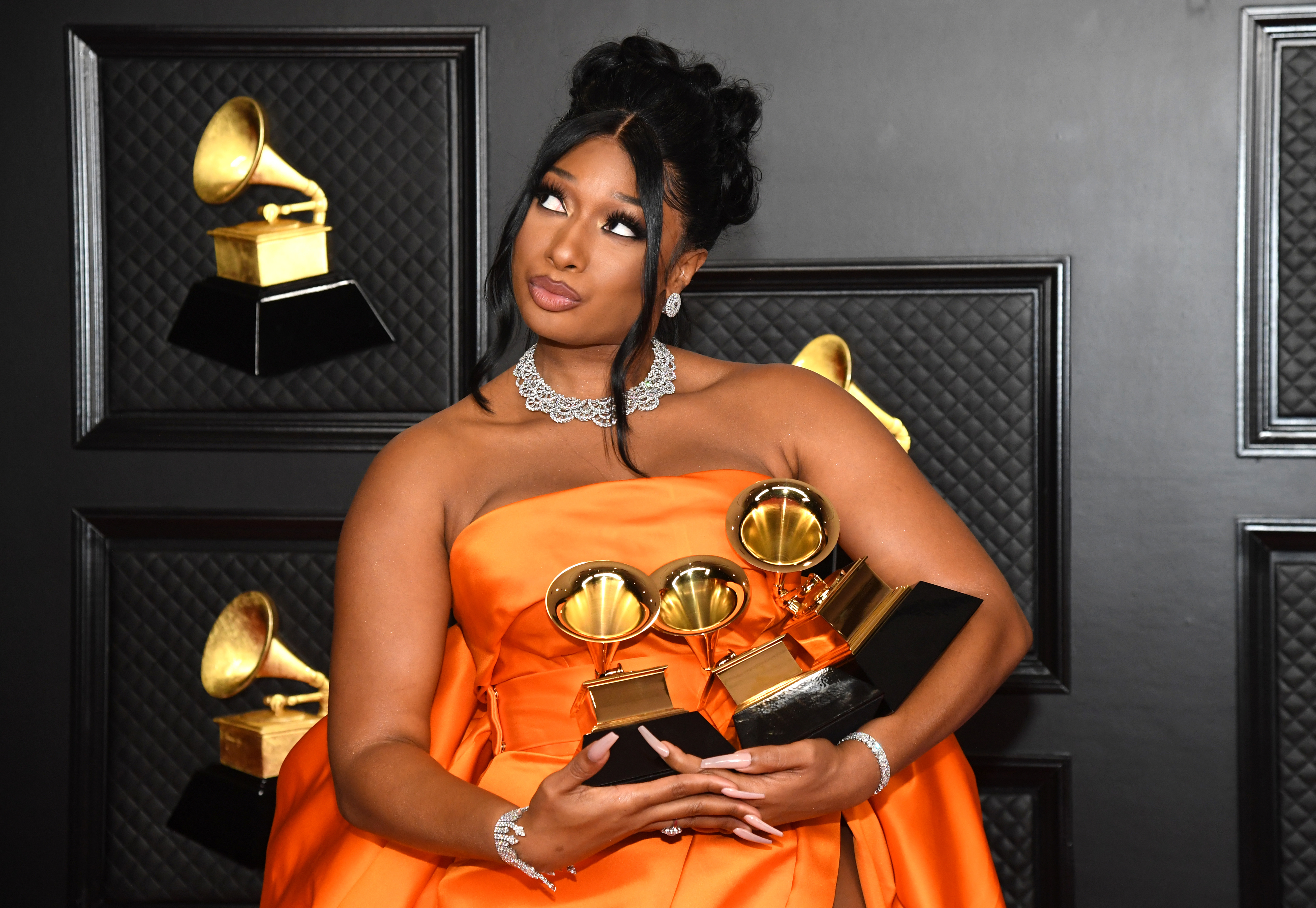Megan Thee Stallion in an orange gown posing with three Grammy awards