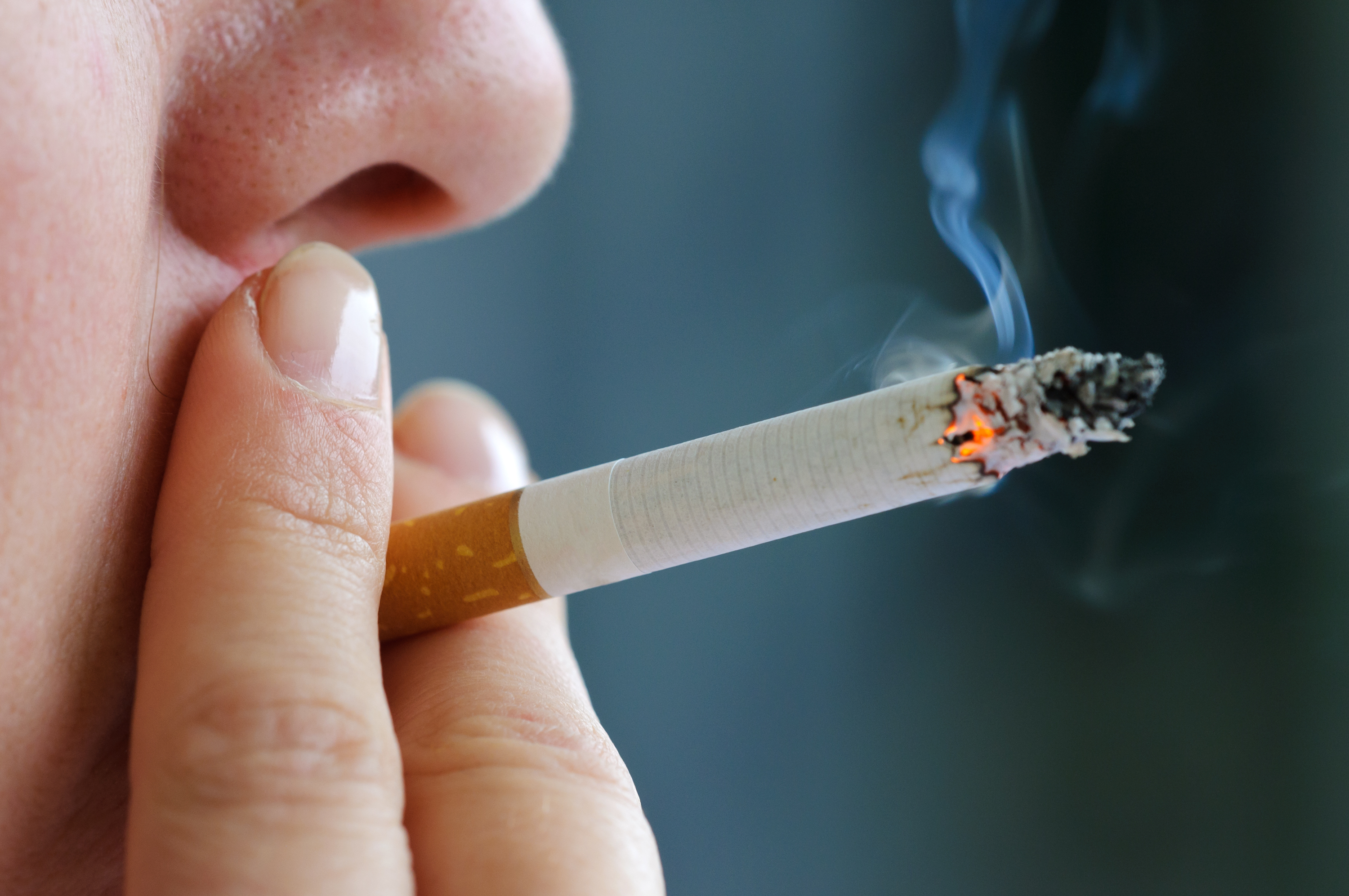Close-up of a person smoking a lit cigarette, with smoke rising from the tip