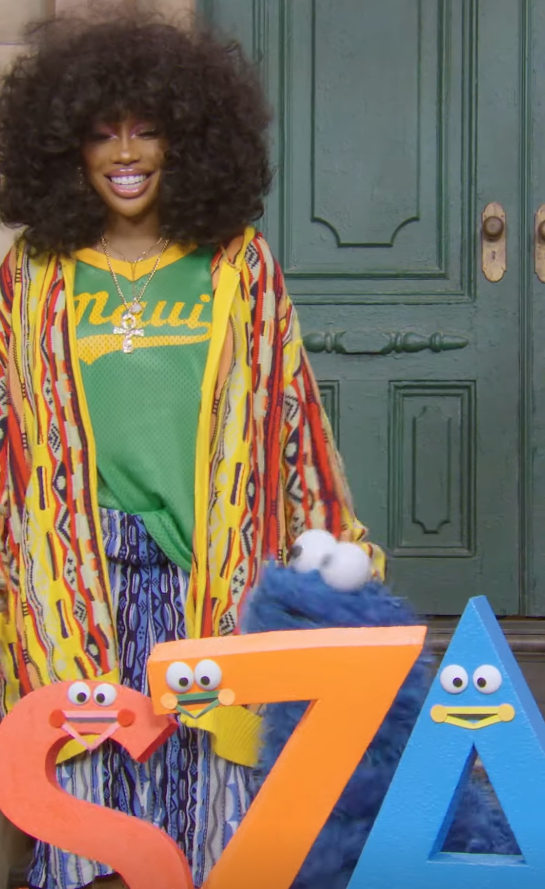 Person on Sesame Street wearing layered patterned clothing with numbers 5, 7, and 4