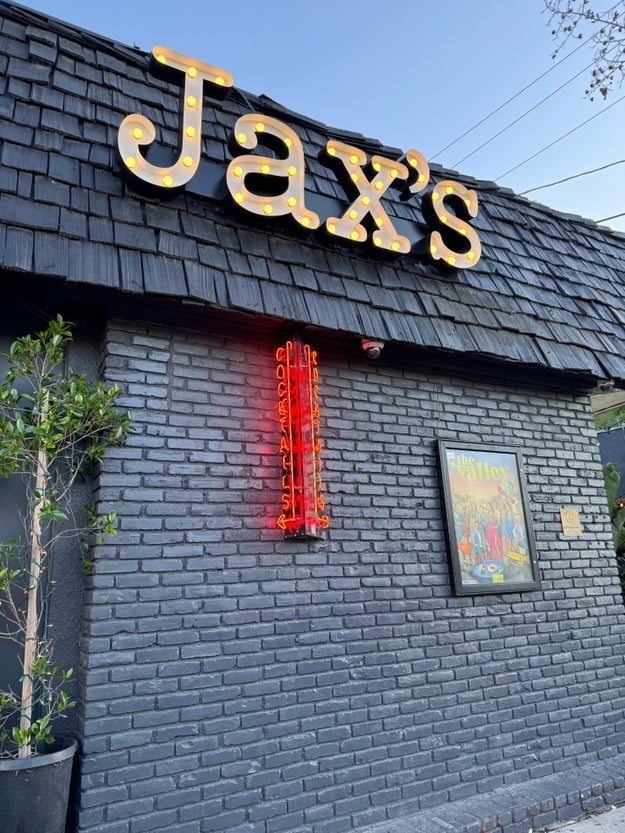 Exterior of Jax&#x27;s restaurant with lit signage and neon light, next to a framed picture on the wall