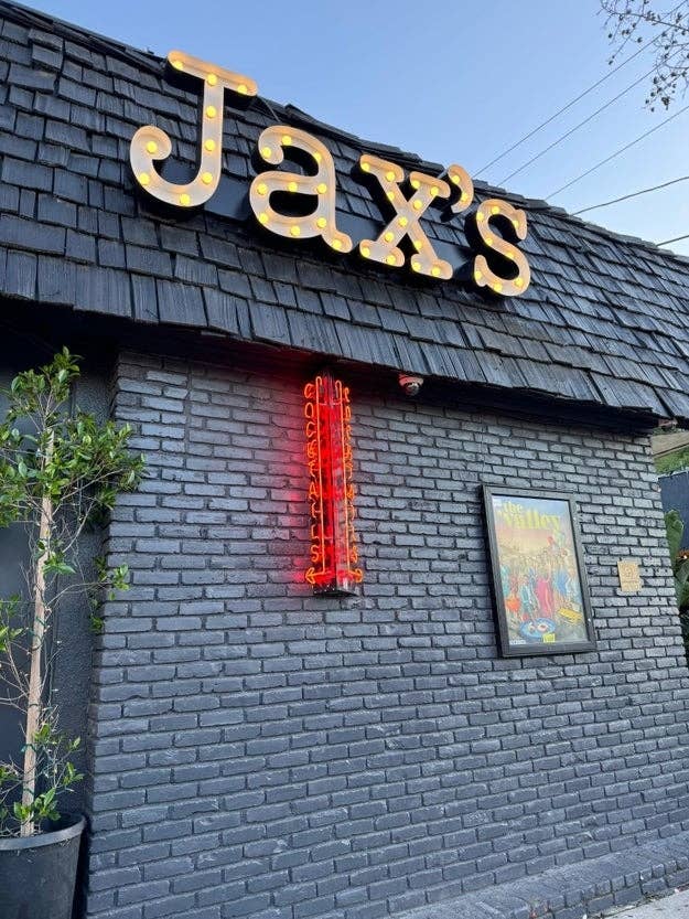 Exterior of Jax&#x27;s edifice  with lit signage and neon light, adjacent  to a framed representation   connected  the wall