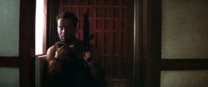 Character from the movie Die Hard holding a gun, expressing tension, in a dimly lit room with window grids