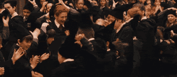 Multitud de estudiantes con togas y birretes celebrando la graduación, levantando sus brazos en el aire en señal de júbilo