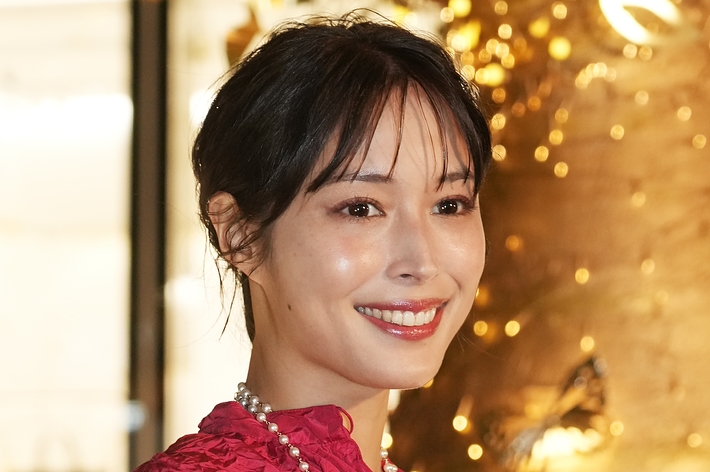 笑顔の女性が金色のアクセサリーをあしらった赤いドレスを着ています。