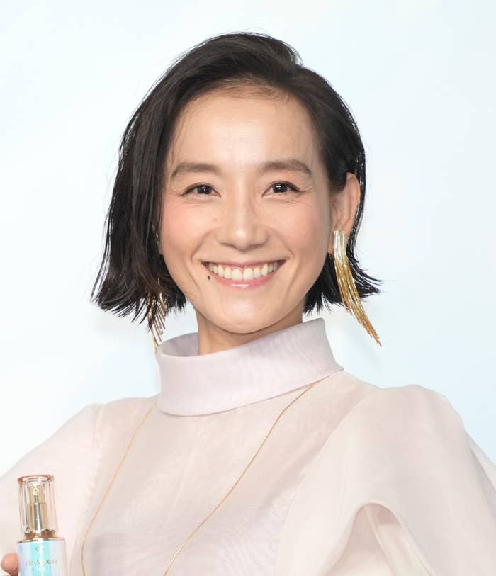 笑顔の女性がカメラを見ていて、ハイネックのトップスとイヤリングを着用しています。