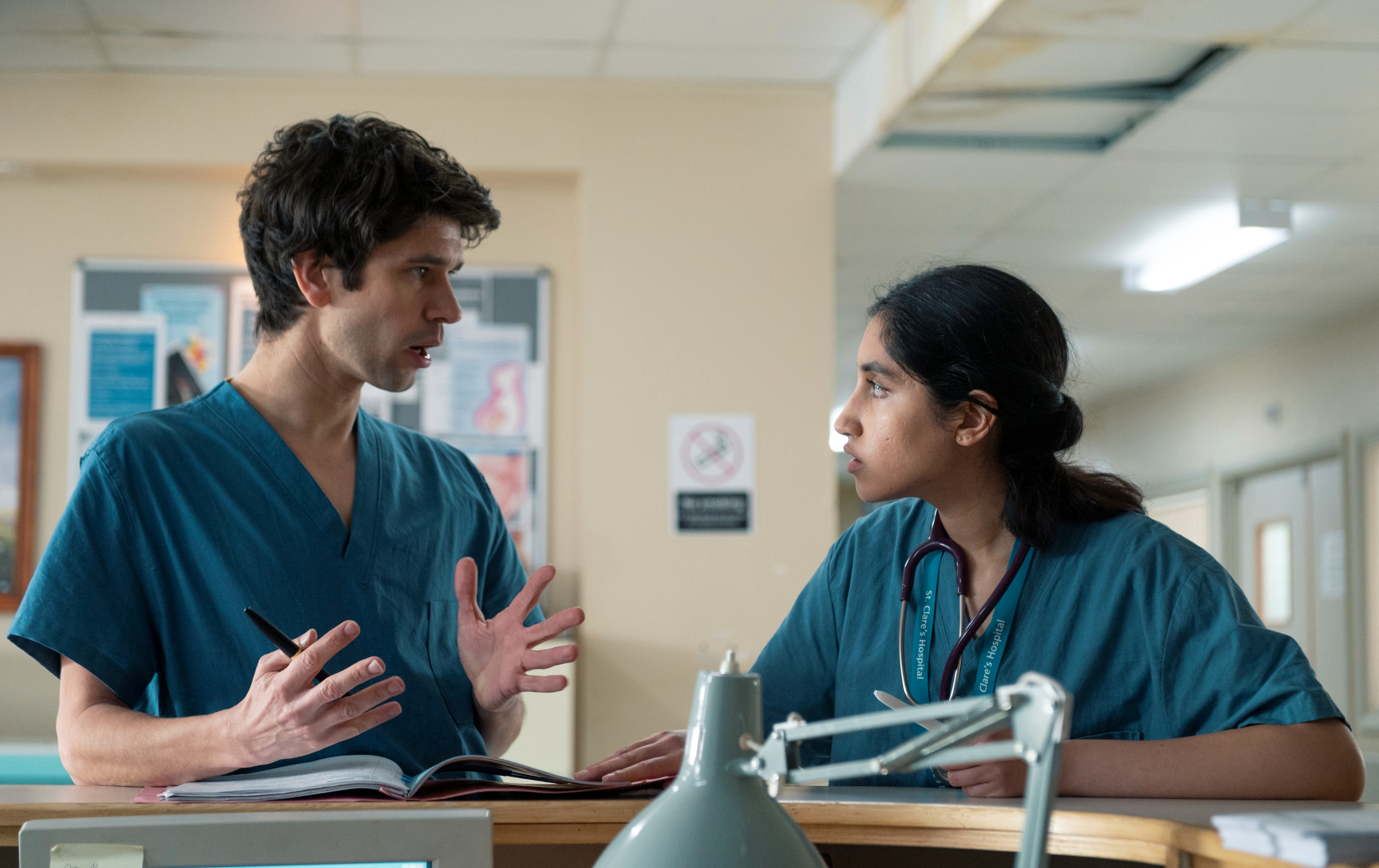 Two actors in medical scrubs engaged in conversation on a hospital set