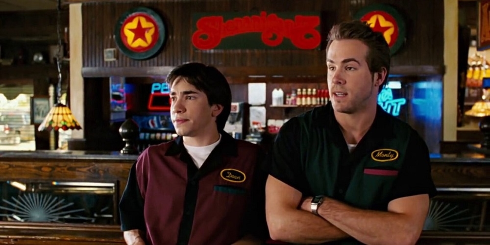 Two characters from a film scene stand behind a bar with logoed shirts, appearing in a conversation