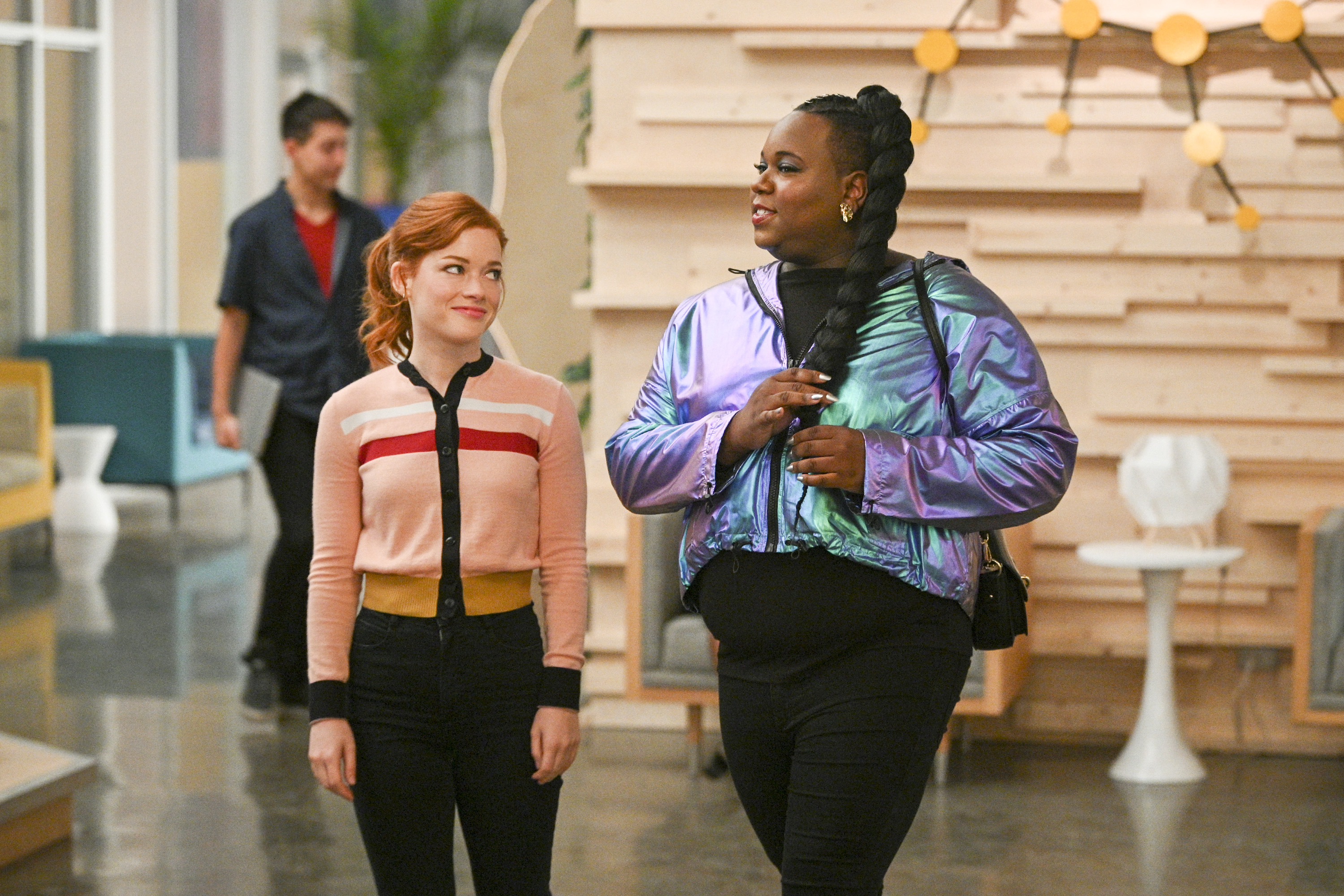 Two characters from a TV show walking and talking in an indoor set with a casual background
