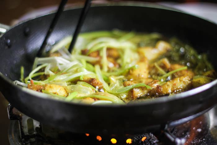 Frying pan on a stove with sizzling chicken and vegetables