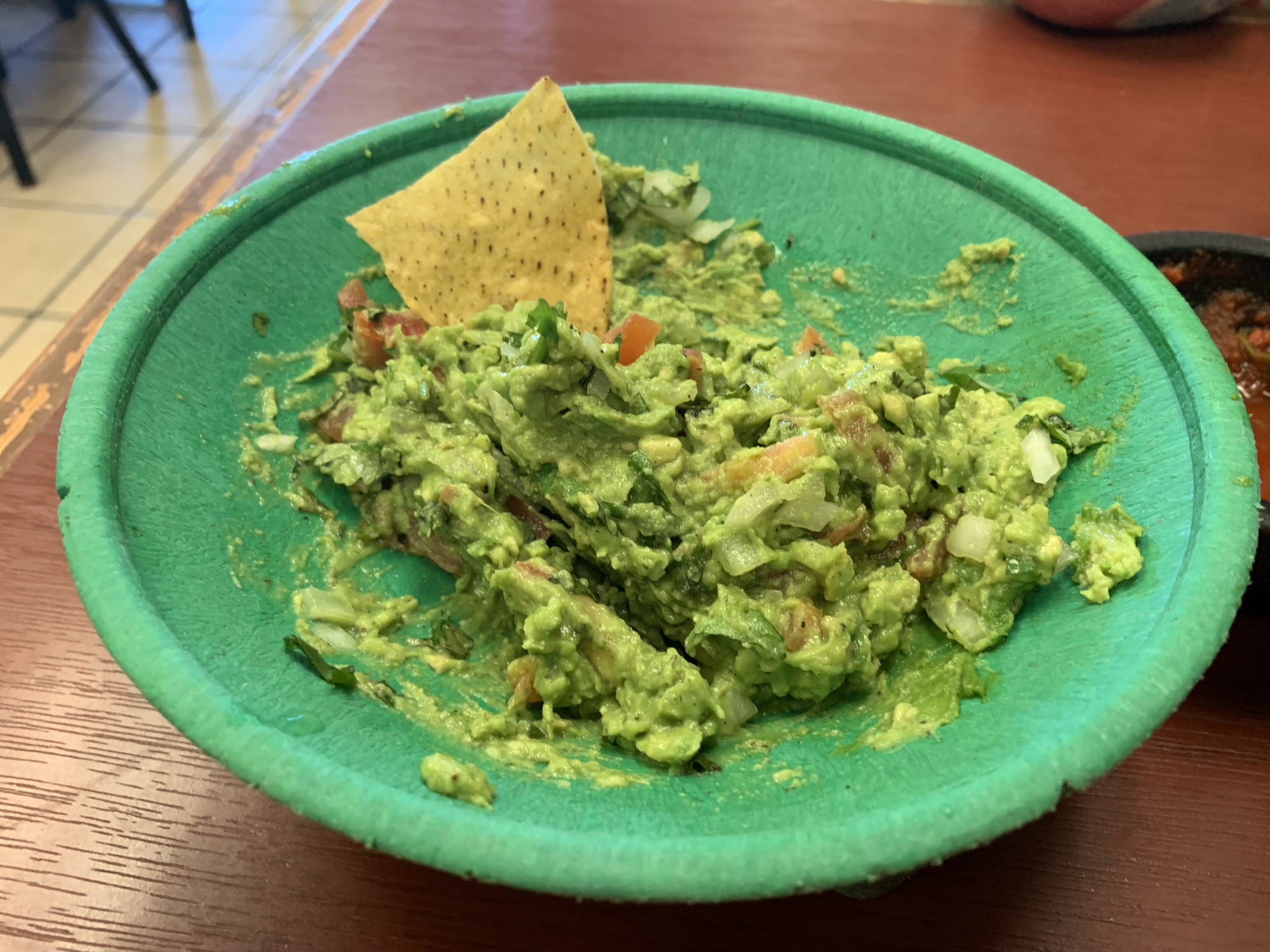 Partially eaten guacamole with a tortilla chip on a green plate