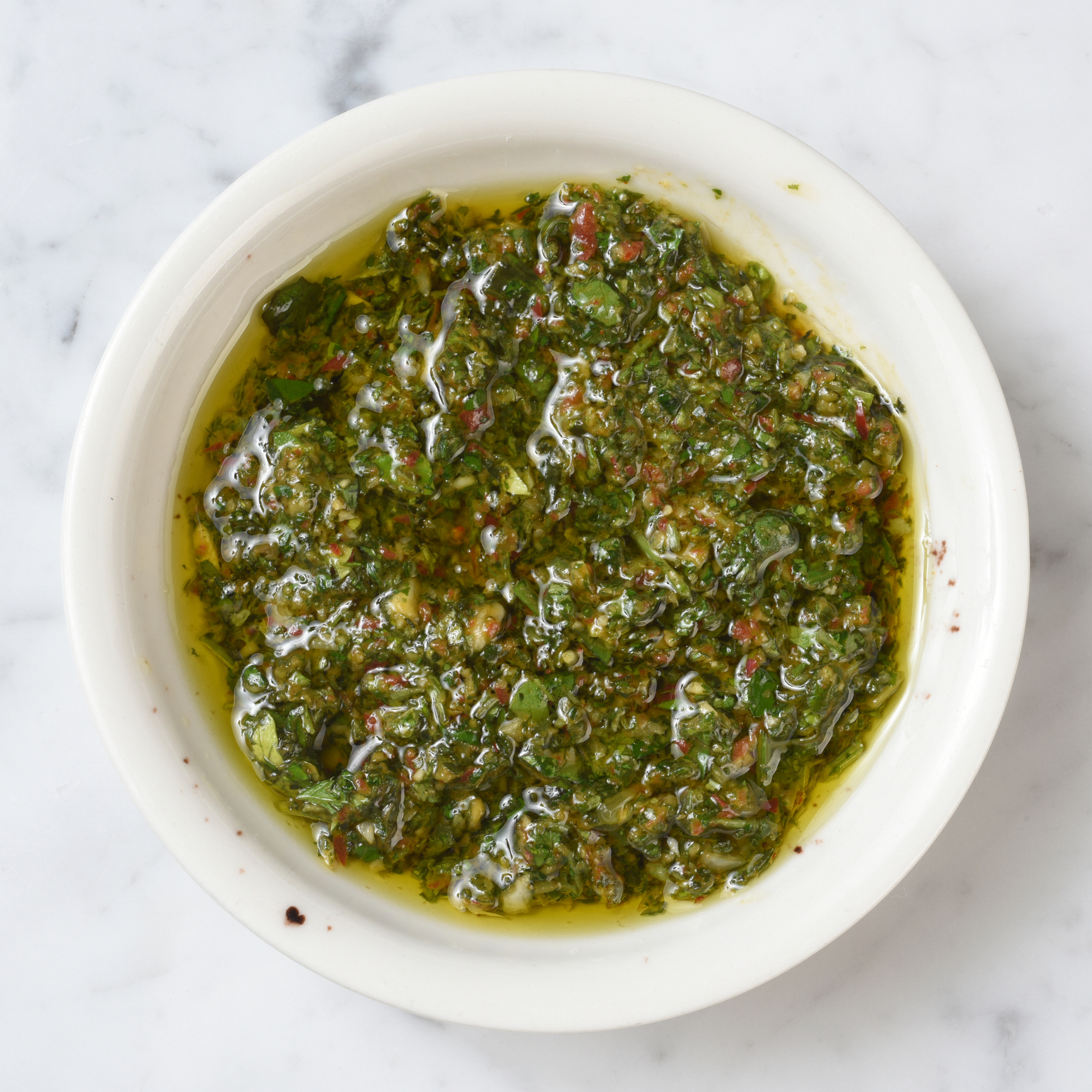 Bowl of chimichurri sauce with herbs and oil visible on a countertop