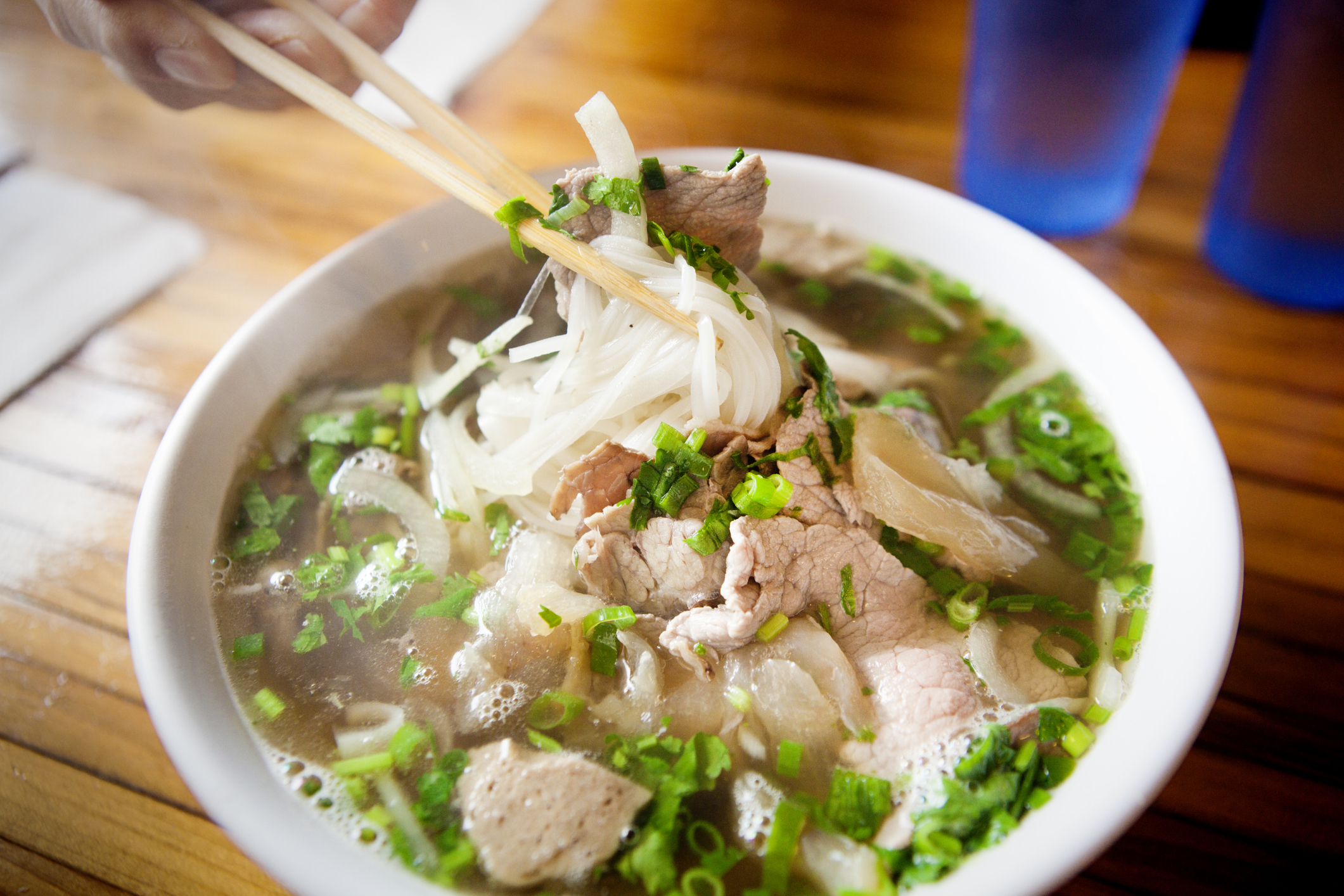 A bowl of pho with chopsticks lifting noodles and slices of beef, garnished with green onions