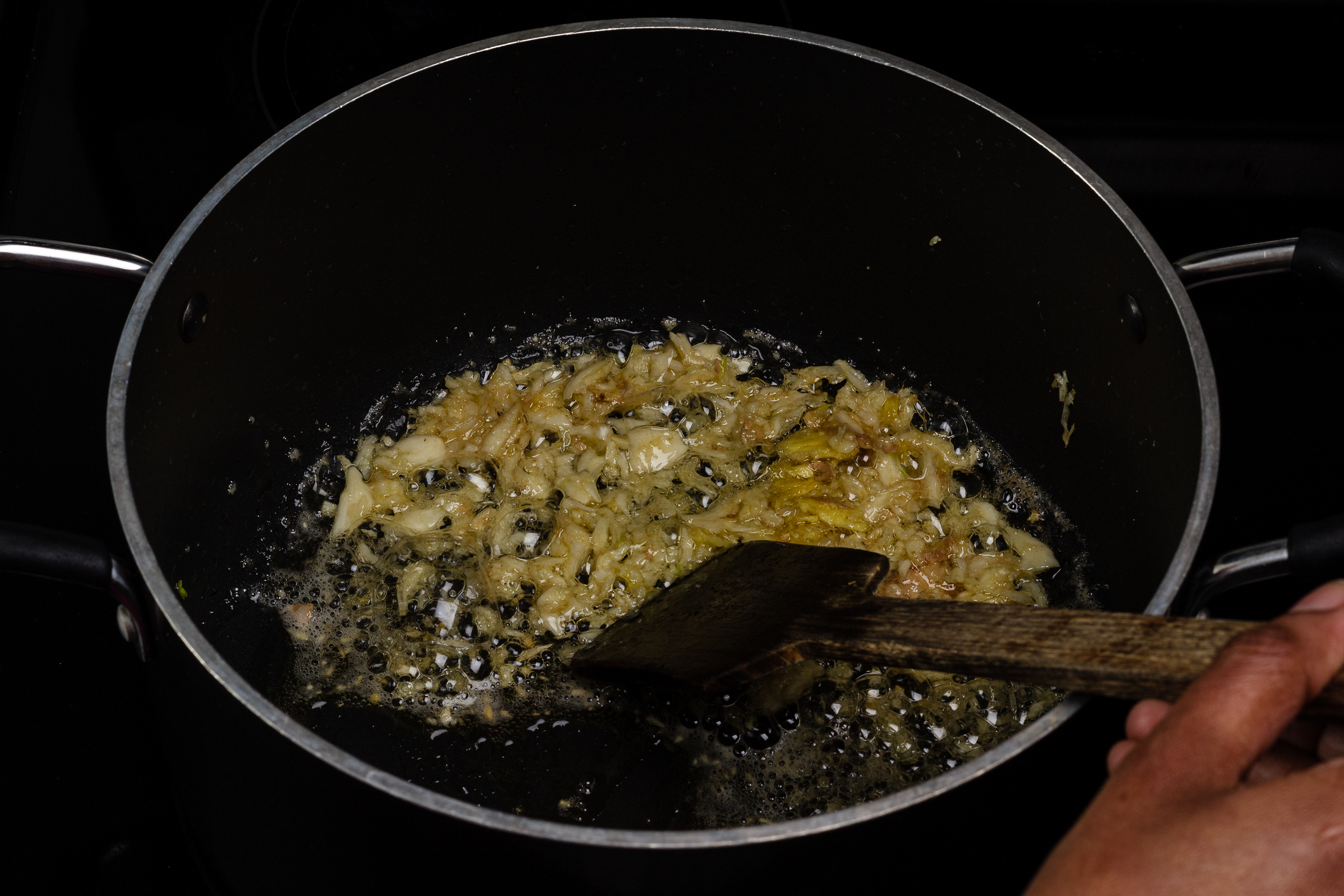 A person is frying onions in a pan with a wooden spatula