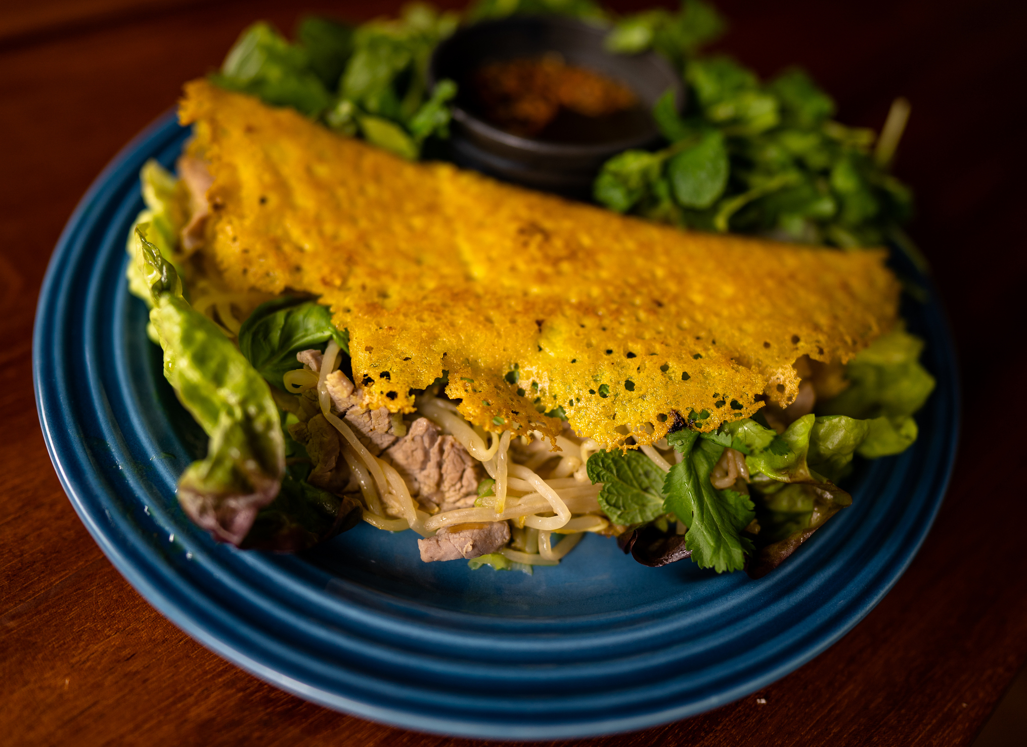 A taco with lettuce and shredded cheese on a blue plate, with a side of sauce