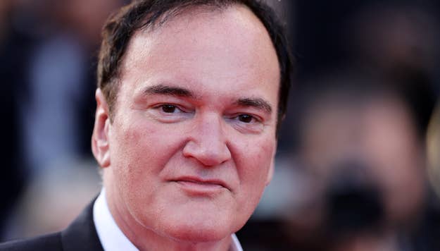 Quentin Tarantino smiling at a formal event in a black suit and tie