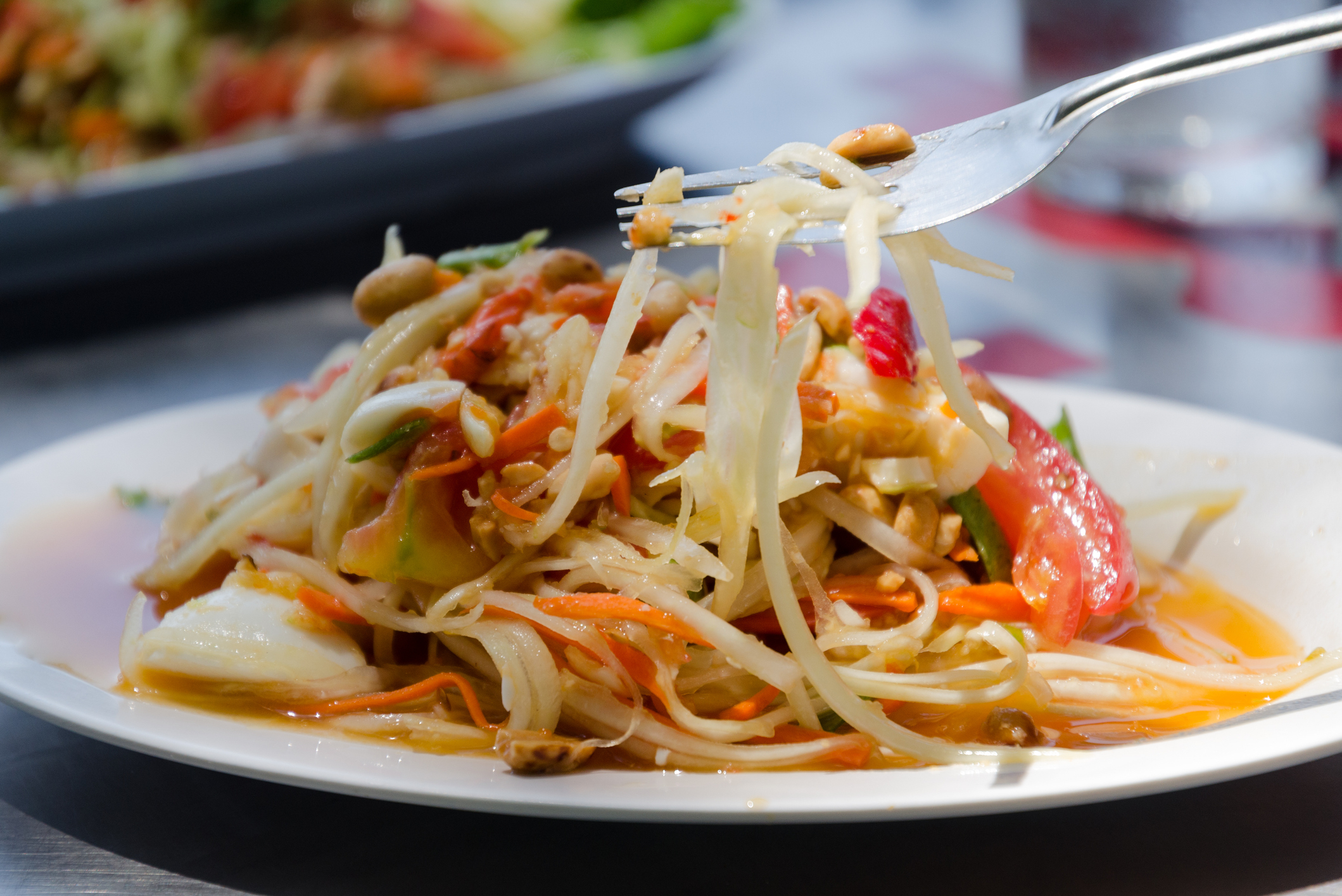 A plate of Pad Thai with a fork lifting some noodles, garnished with peanuts and mixed vegetables