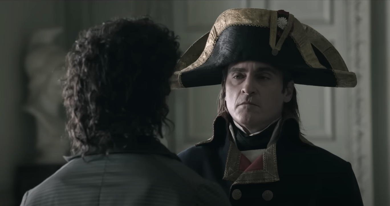 Joaquin Phoenix as Napoleon looking at another person stoicly