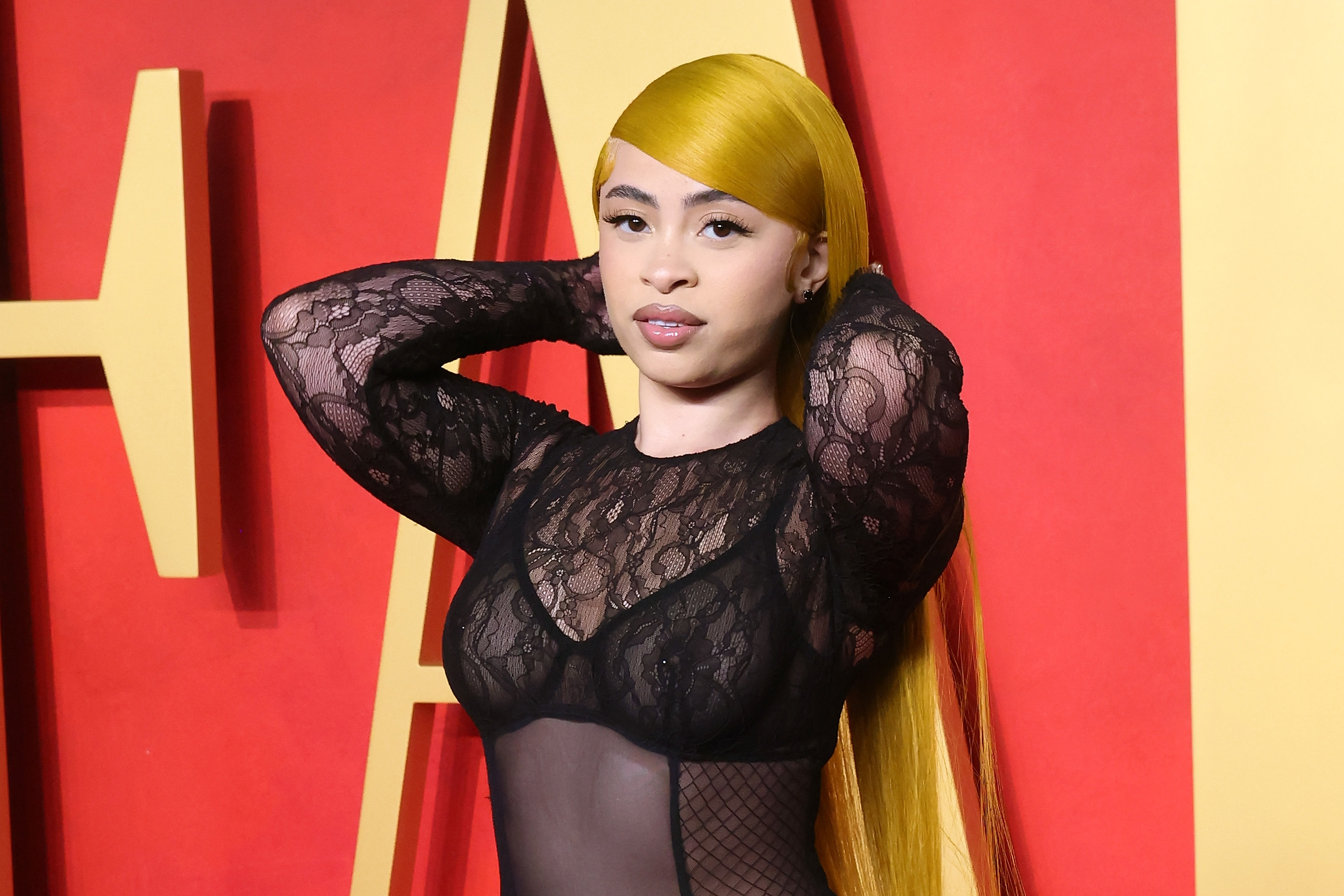 Ice Spice in a sheer lace top and long yellow hair posing on the red carpet