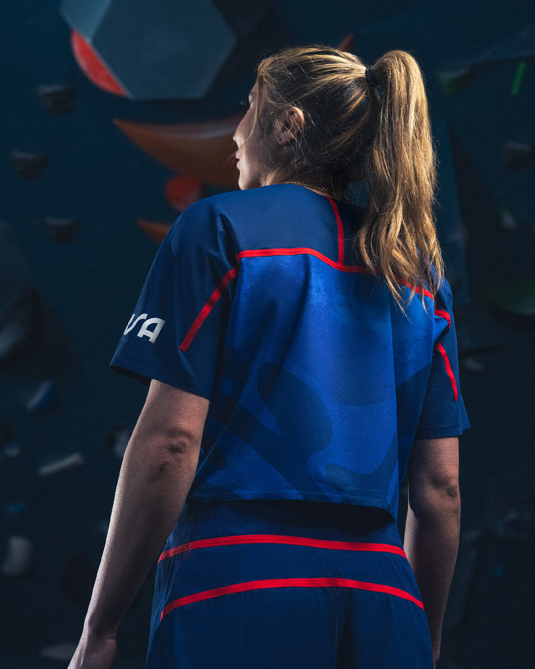 Woman in sportswear with ponytail standing in front of climbing wall, facing away