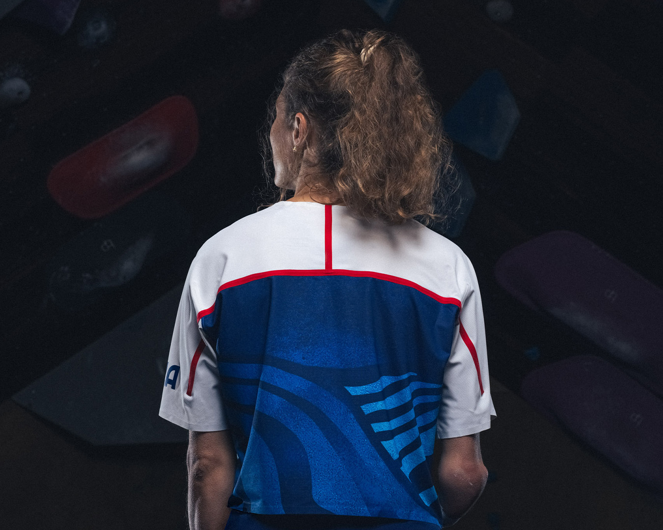 Person in a sports jersey with a ponytail standing in front of a climbing wall