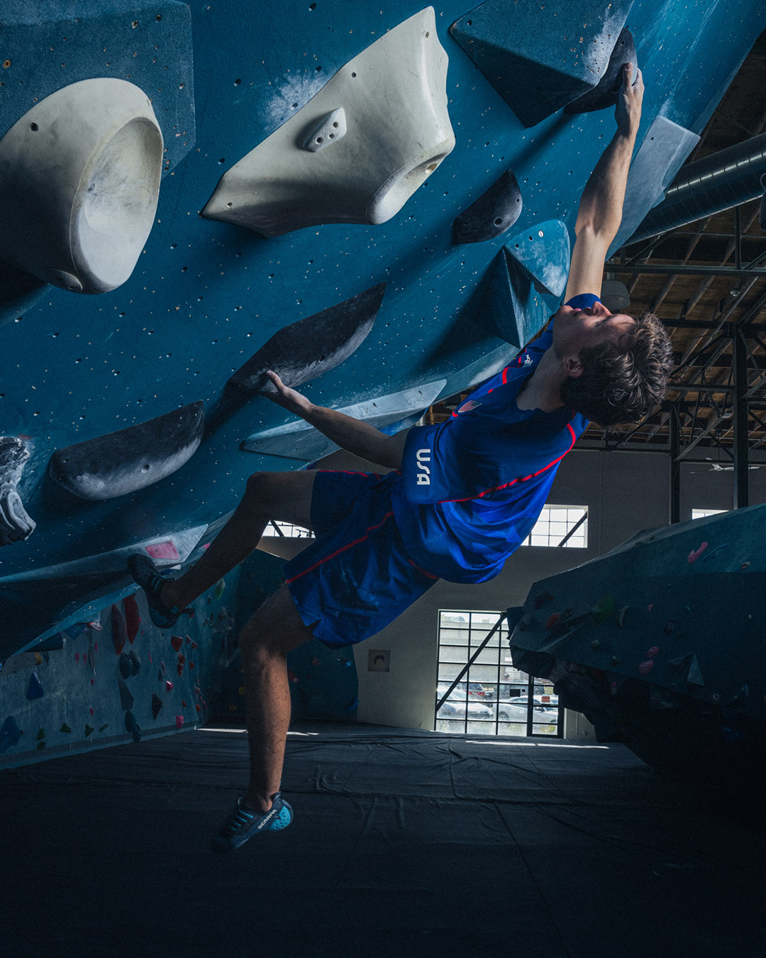 Person in athletic wear rock climbing indoors, reaching for a hold on an inclined wall