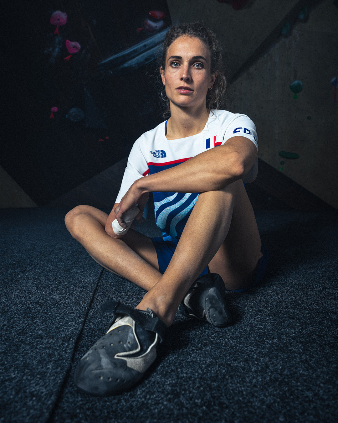 Woman in a climbing gym wearing a sports jersey and holding climbing shoes