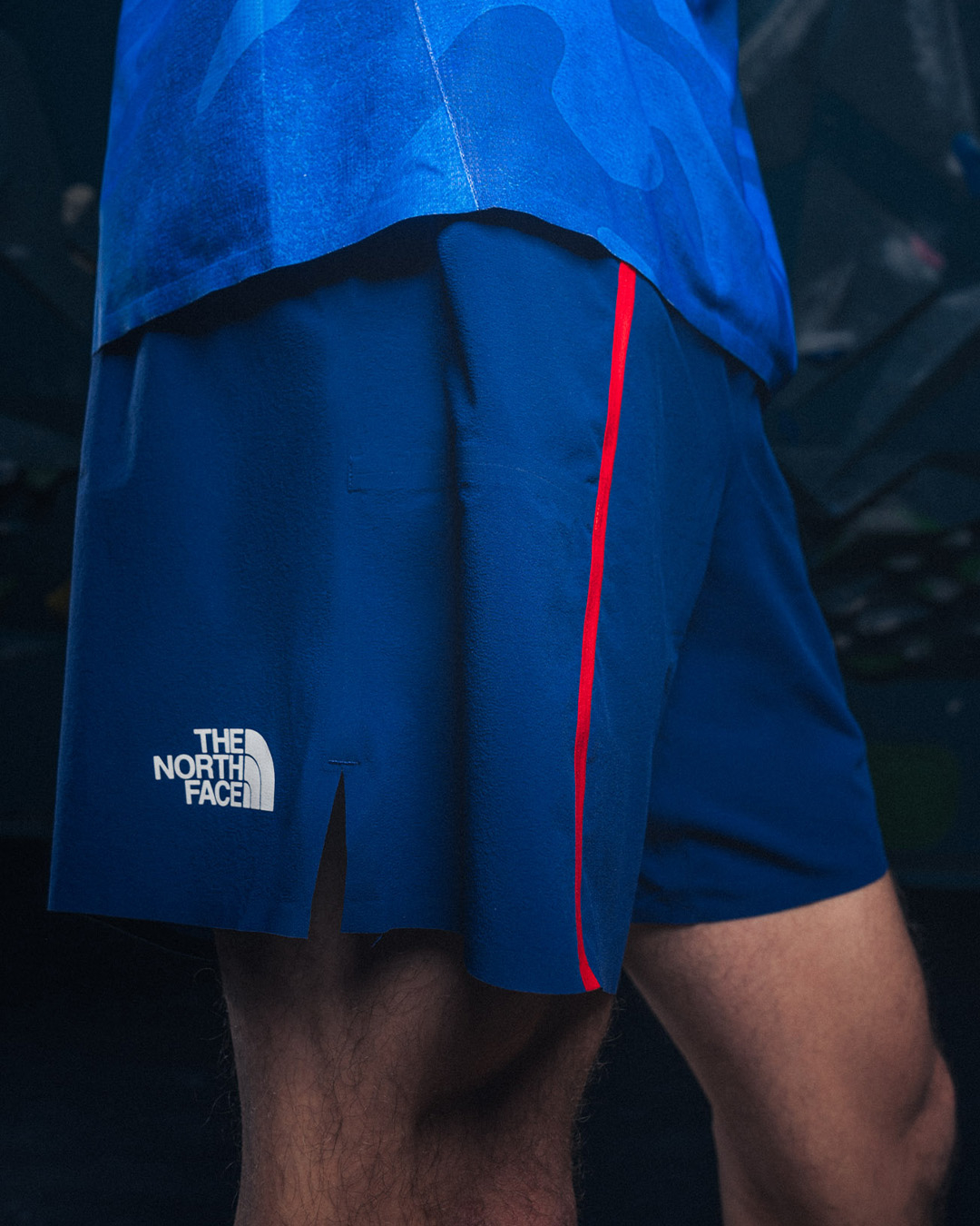 Close-up of a person wearing blue The North Face shorts with logo, featuring a red stripe