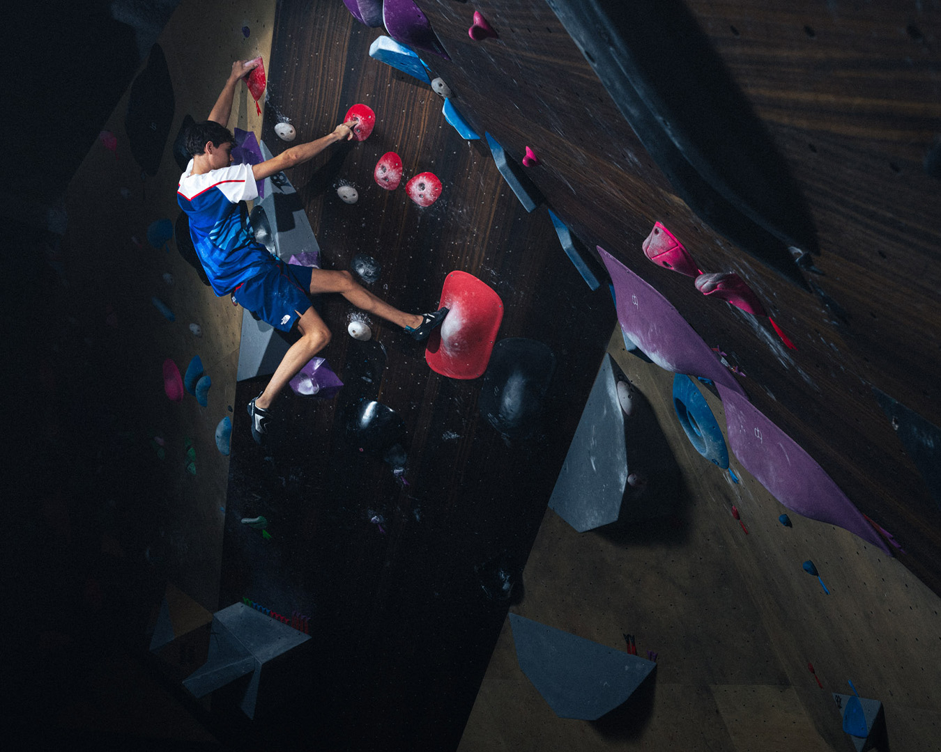 Person indoor rock climbing, reaching for a hold, in athletic attire