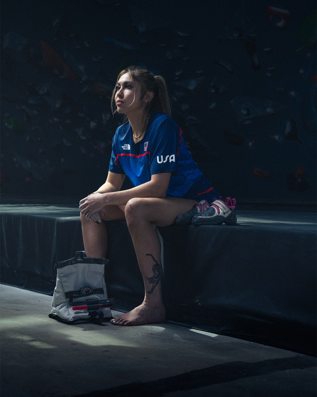Athlete in a USA jersey sits beside climbing gear, focused and contemplative before a competition