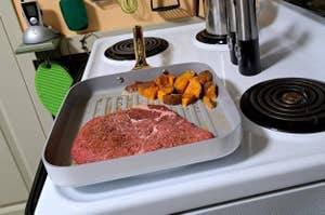 Raw steak and diced sweet potatoes on a baking tray, ready to be cooked, on a kitchen stove