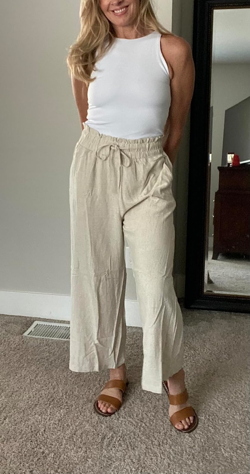 Woman in white tank top and beige linen pants with brown sandals, showcasing a casual outfit