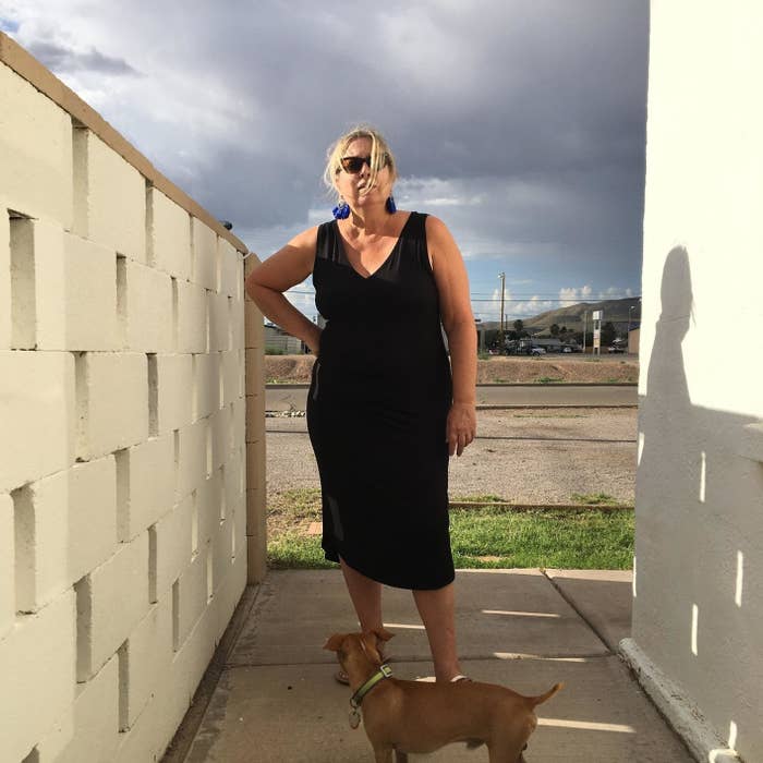 Woman in the black sleeveless dress stands with a dog on a leash