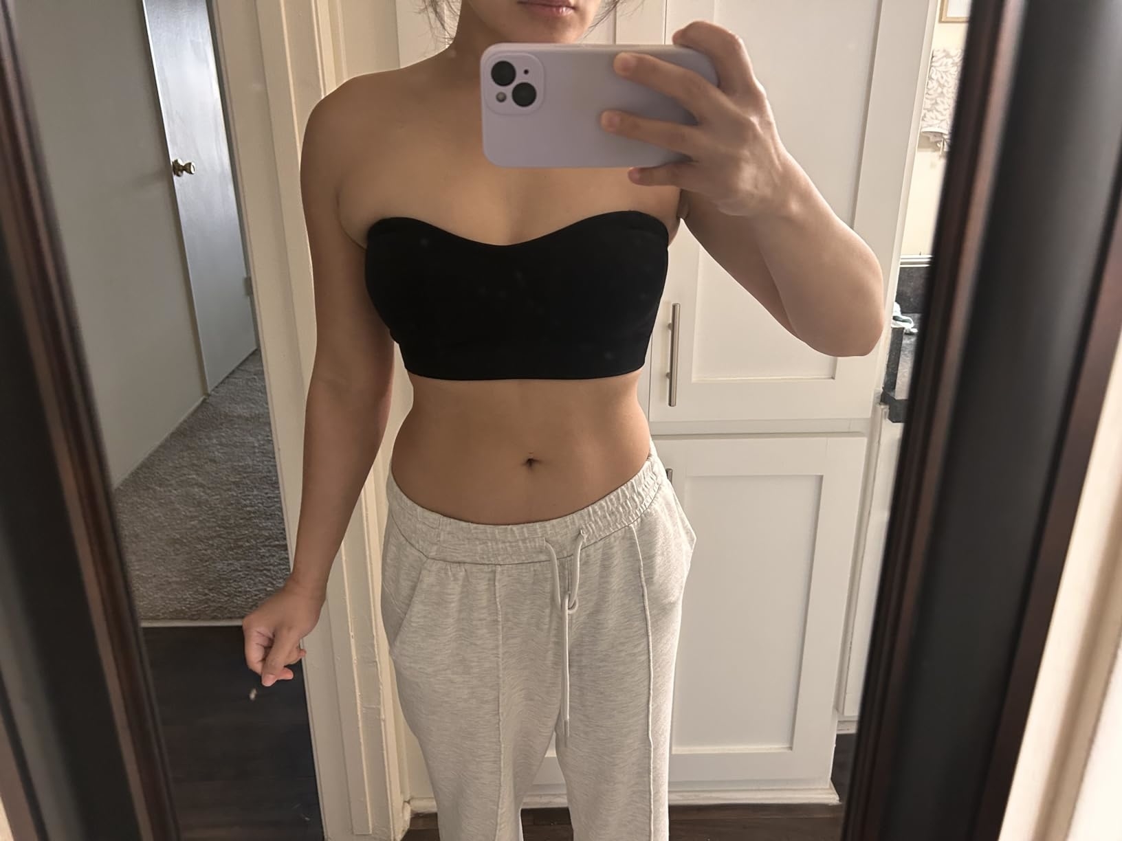 reviewer in mirror taking a photo wearing the black strapless bandeau bra and grey sweatpants