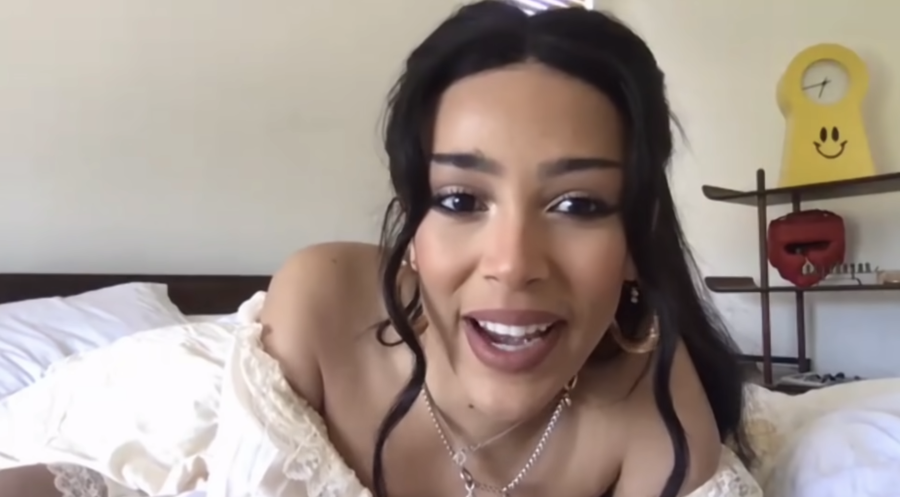 Woman in a white off-the-shoulder top with hoop earrings, smiling during a video call