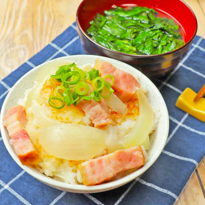 ご飯の上に玉ねぎと厚切りベーコンがのった丼と椀に入った緑の野菜の写真です。
