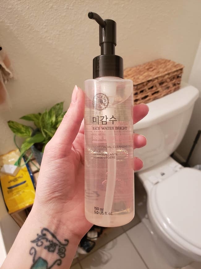 Person holding a bottle of Rice Water Bright facial cleanser in a bathroom setting