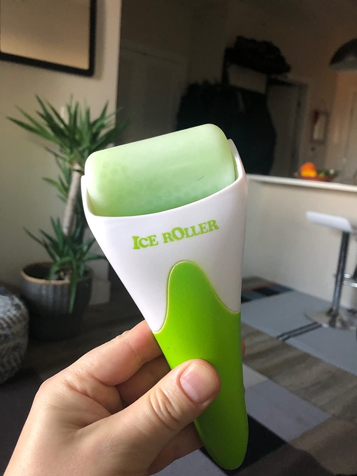 Hand holding an ice roller skincare tool, with indoor background
