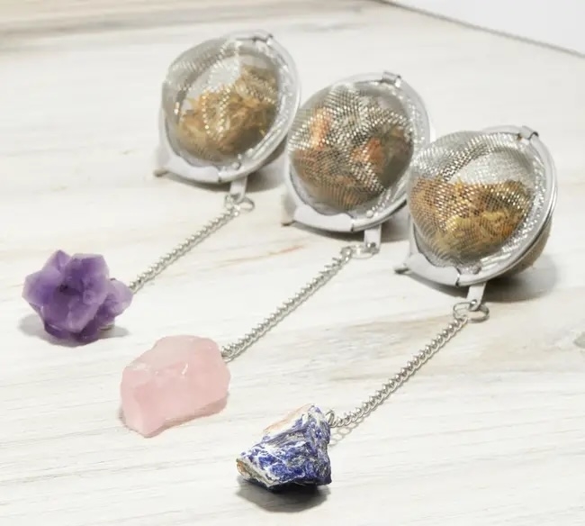 Tea infusers with gem-shaped pendants on a chain resting on a wooden surface