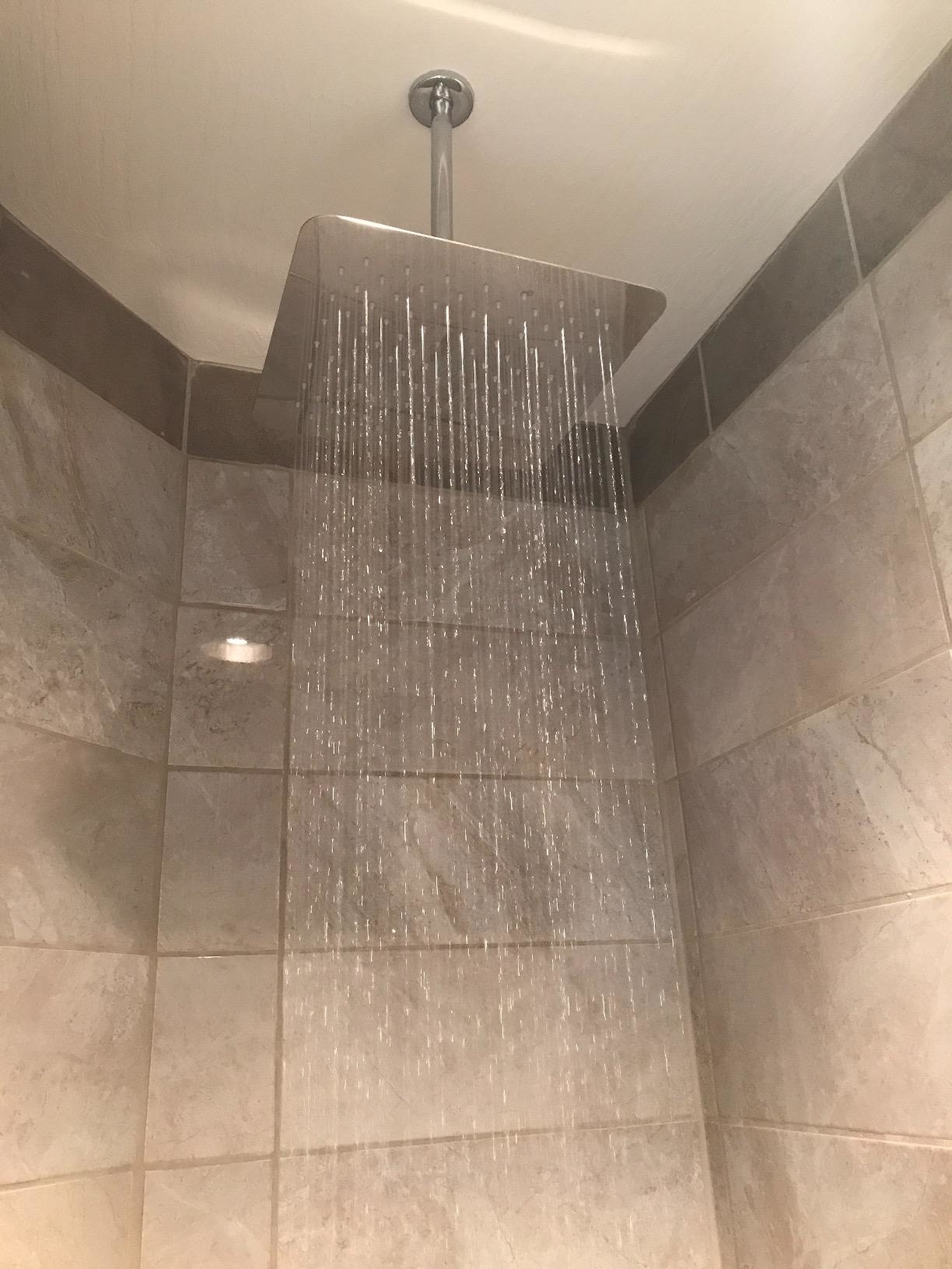 Modern rainfall showerhead streaming water in a tiled shower stall
