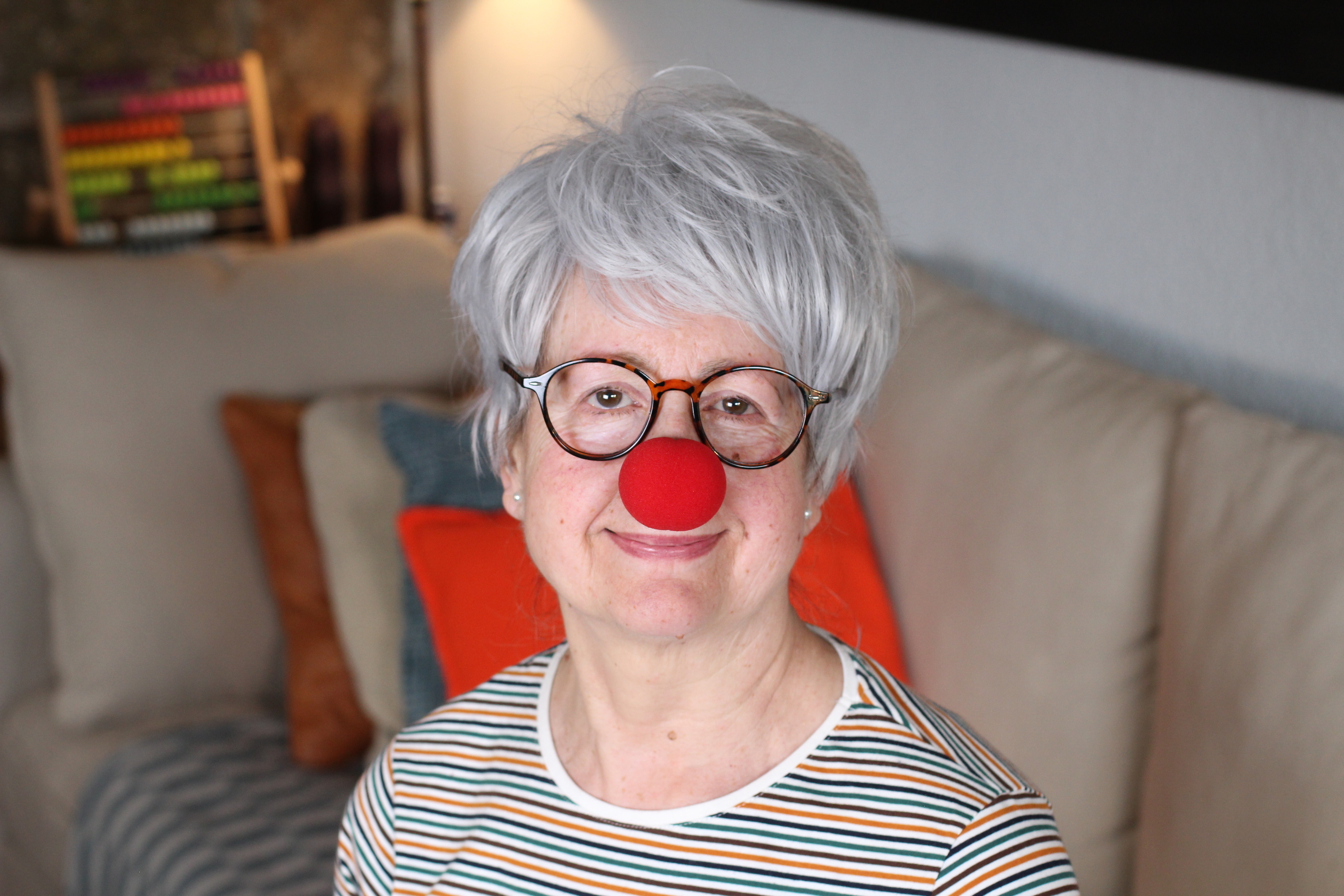 Woman with a red clown nose, glasses, and a striped shirt smiles at the camera